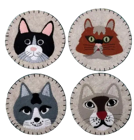 Four circular cat face patches on a green cutting mat with grid lines.