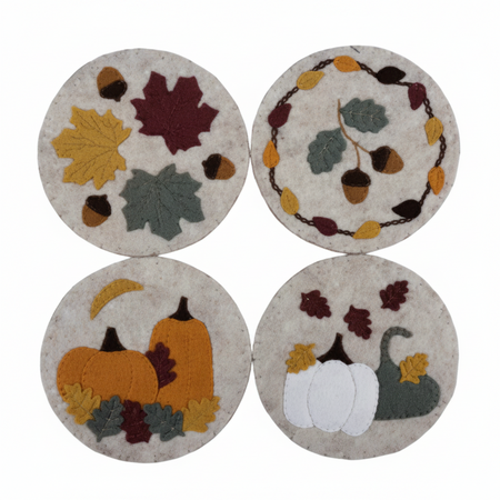 Four round felt coasters with autumn-themed designs including maple leaves, acorns, pumpkins, and white pumpkins, arranged in a 2x2 grid on a white background.